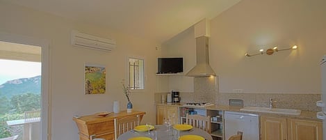 A modern kitchen with a dining area, a TV mounted above the counter, and a view of the outdoors.