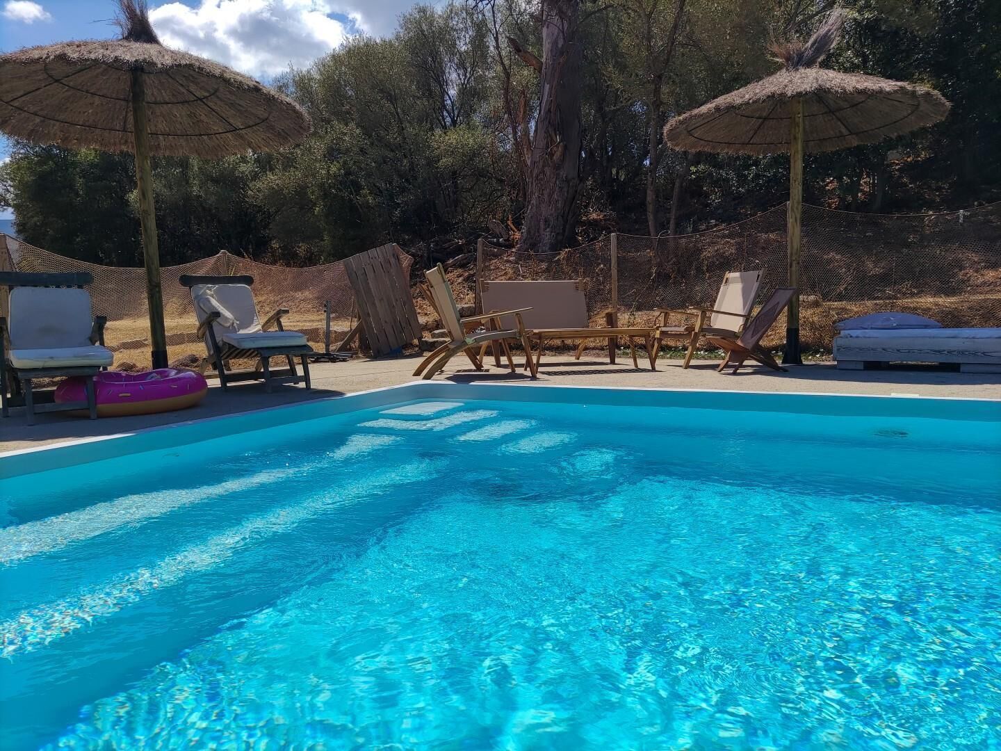 Una piscina con agua azul cristalina, rodeada de sillas de descanso y sombrillas.