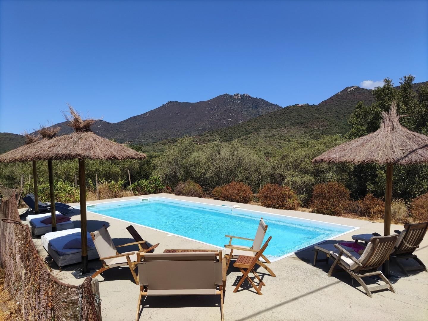 A pool with lounge chairs and thatched umbrellas, surrounded by greenery and mountains.