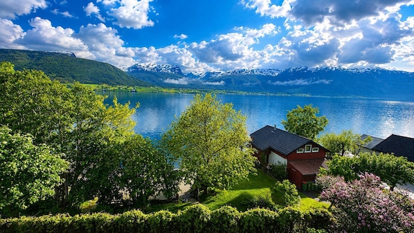 A lakeside property with a red house, lush greenery, and mountains in the background.