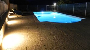 Una piscina con un borde empinado, rodeada de una cerca e iluminada por luces artificiales.