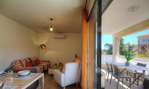 Ein gemütlicher Wohnbereich mit einer Couch, Esstisch und Stühlen, einem Deckenventilator und Blick ins Freie.