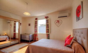 Ein Schlafzimmer mit einem Bett, einem Schminktisch, einem Spiegel, einem Fenster mit Vorhängen und einem Wandheizkörper.