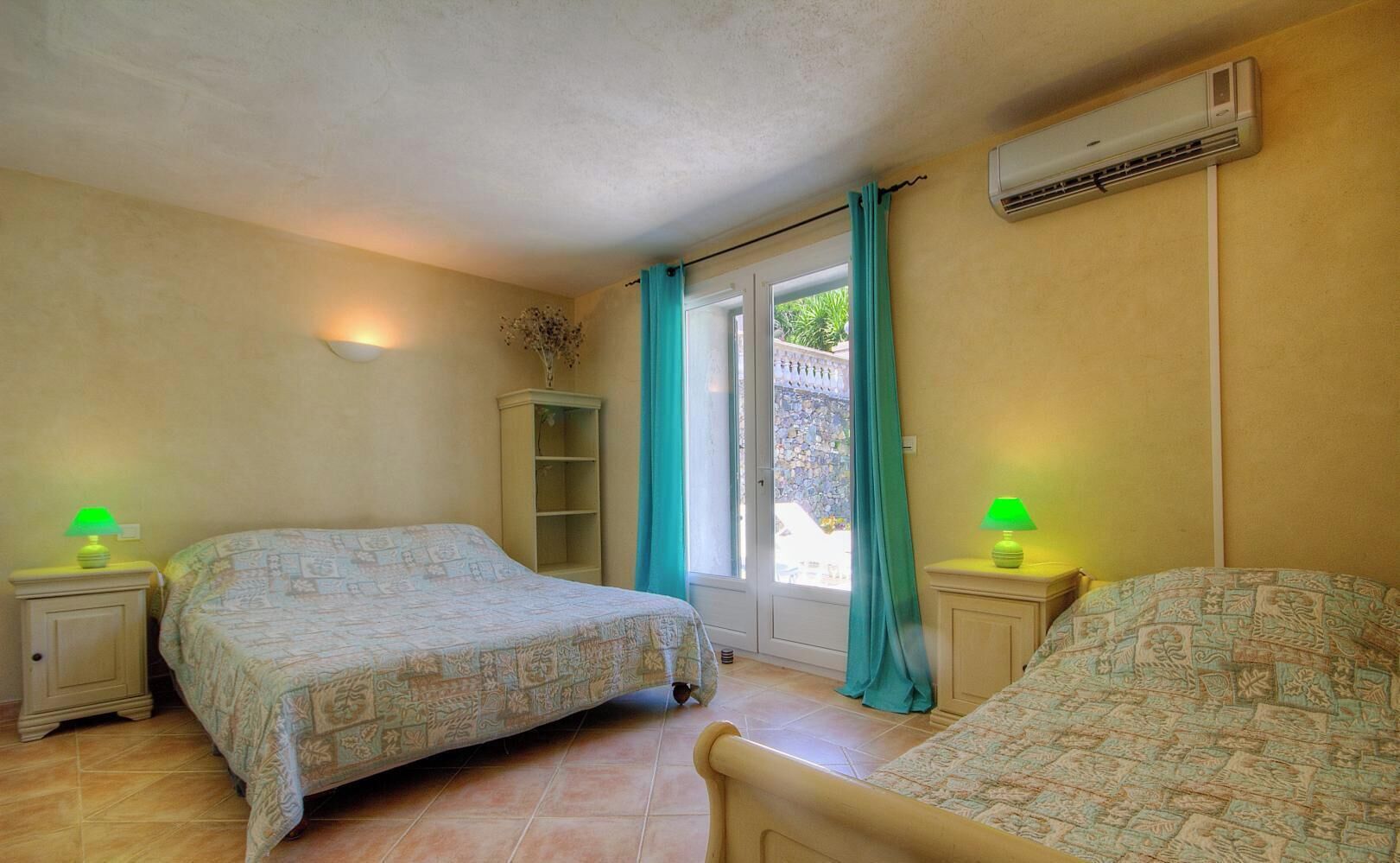 A bedroom with two beds, a window with curtains, an air conditioning unit, and a small cabinet.