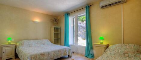 A bedroom with two beds, a window with curtains, an air conditioning unit, and a small cabinet.