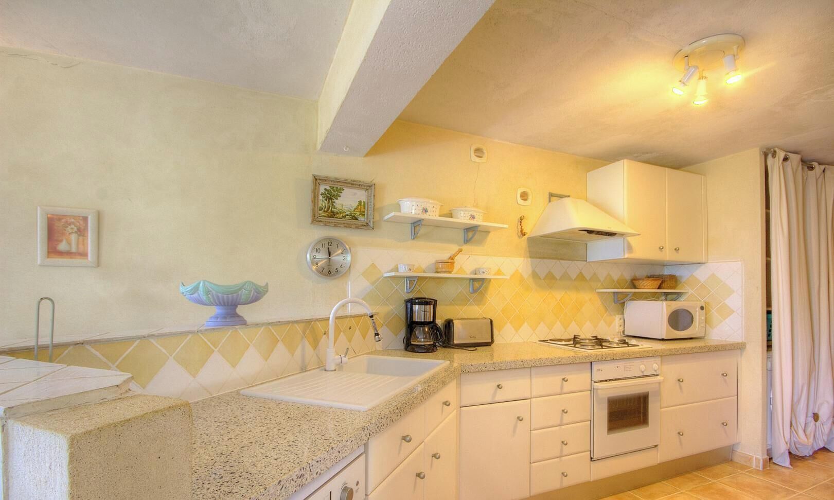 A kitchen with a sink, countertop, stove, and cabinets.