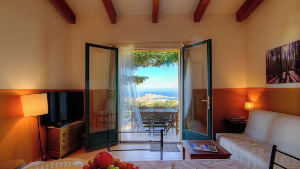 Une pièce avec une télévision, une table garnie de fruits, un canapé et un balcon avec vue.
