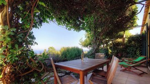 Une table en bois, des chaises, une bouteille et des verres, le tout entouré de verdure et offrant une vue agréable.