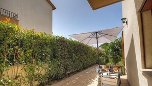A patio with a table set for breakfast, a large umbrella, and a hedge along the wall. - Studio Molini - ALBITRECCIA (ALBITRECCIA)