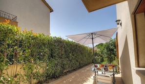 Eine Terrasse mit einem für das Frühstück gedeckten Tisch, einem großen Sonnenschirm und einer Hecke entlang der Mauer.