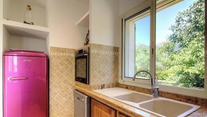 A kitchen with a pink refrigerator, a microwave, a dishwasher, and a window with a view of greenery. - Santa Maria - PIETRALBA (PIETRALBA)