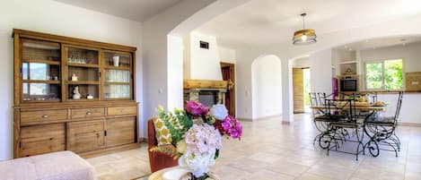A spacious living area with a wooden cabinet, a dining table with chairs, and a fireplace.