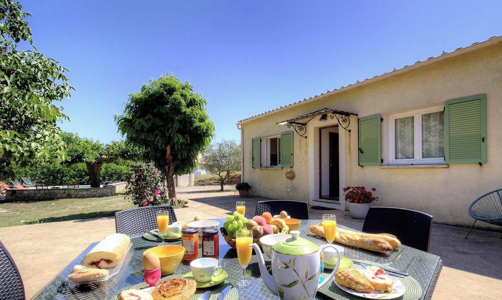An outdoor dining area with a table set for breakfast, including bread, fruit, and beverages.
