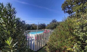 A rectangular pool with a wooden deck and a white fence, surrounded by dense greenery and trees. - 15238 - SOTTA - Gîte (SOTTA)