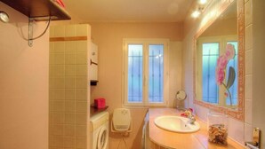 Een badkamer met een wasmachine, een wastafel, een spiegel en een raam met gezandstraald glas.