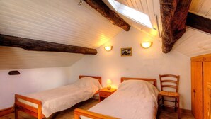 Una stanza piccola e accogliente con due letti di legno, una sedia di legno, un comodino con una lampada e un armadio di legno.
