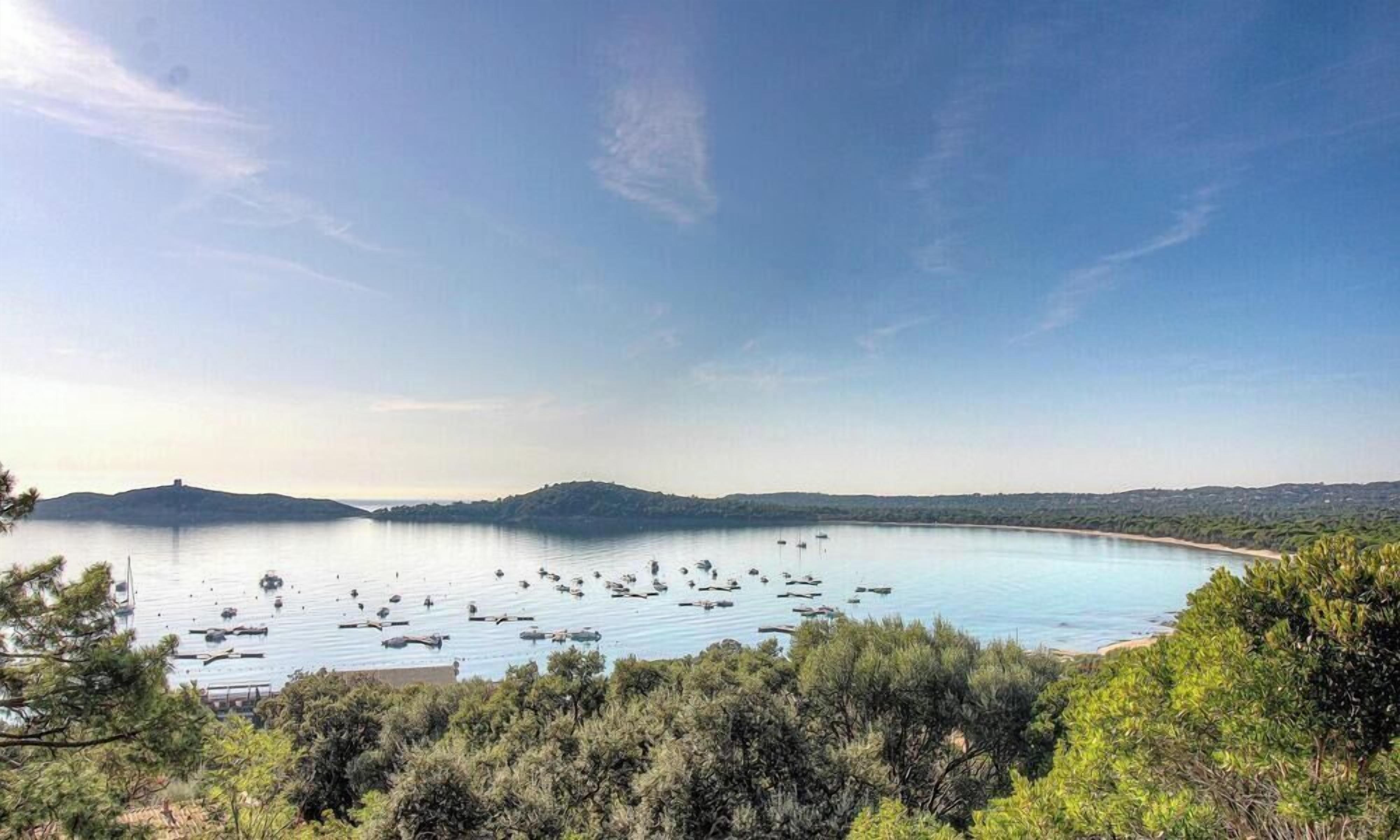 A coastal landscape with a bay, boats, and dense greenery.