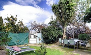 Un jardín con una verja blanca, sillas verdes y una mesa.