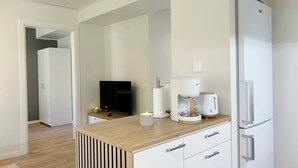 Uma cozinha moderna com bancada de madeira, armários brancos, frigorífico embutido, máquina de café e televisão de ecrã plano.