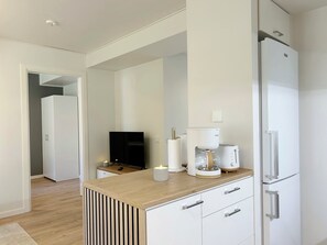 Eine moderne Küche mit Holzarbeitsplatte, weißen Schränken, einem eingebauten Kühlschrank, einer Kaffeemaschine und einem Flachbildfernseher.