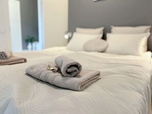 A neatly made bed with a folded towel and a small item on top, a headboard with pillows, and a door leading to another room.