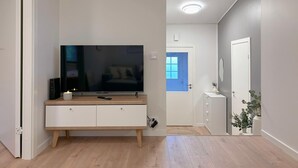 Uma sala de estar moderna com uma televisão de tela plana, um armário de madeira e uma porta azul ao fundo.