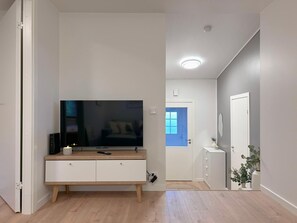 A modern living room with a flat-screen TV, a wooden cabinet, and a blue door in the background.