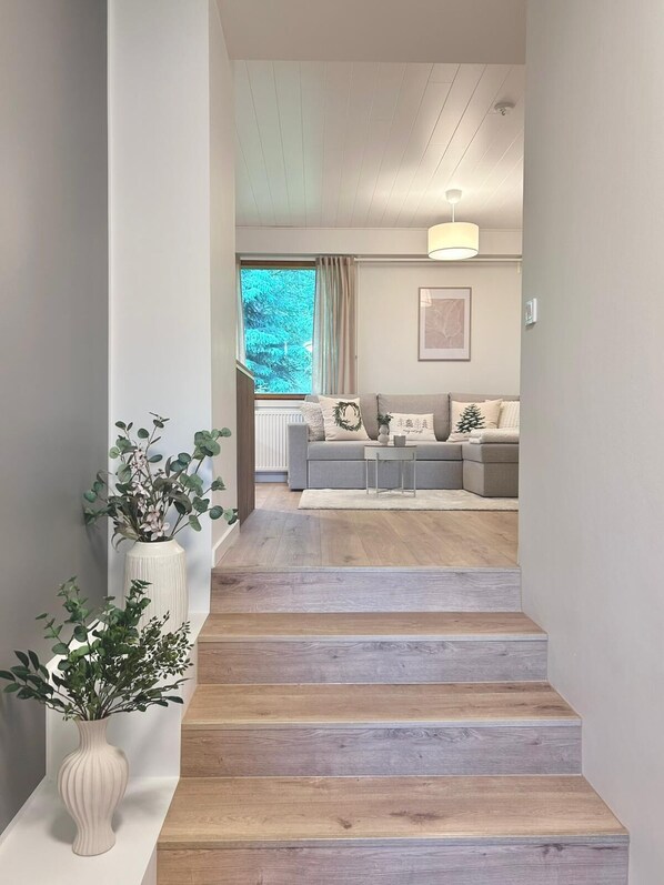 A staircase leading to a living room with a grey sofa, a small table, and a window with curtains.