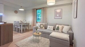 Uma sala de estar moderna com um sofá cinza, uma mesa de centro redonda e uma área de jantar com mesa e cadeiras.