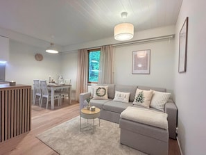 A modern living room with a grey sofa, a round coffee table, and a dining area with a table and chairs.