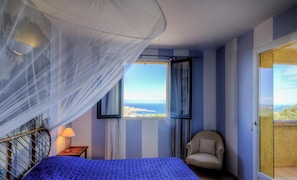 Ein Schlafzimmer mit Bett, Stuhl, Fenster mit Blick und Balkontür.
