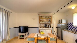 Ett kompakt kök med ett matbord, stolar, en tv och ett kylskåp.