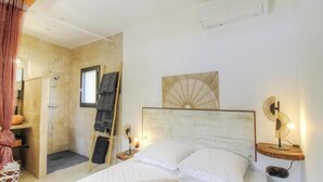 Un dormitorio con cama, mesita de noche, perchero para toallas y zona de ducha.
