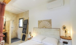 Ein Schlafzimmer mit Bett, Nachttisch, Handtuchhalter und einer Dusche. An der Wand ist ein Ventilator befestigt.