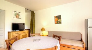 Una habitación con una mesa redonda, un sofá, un televisor sobre un mueble y obras de arte en las paredes.