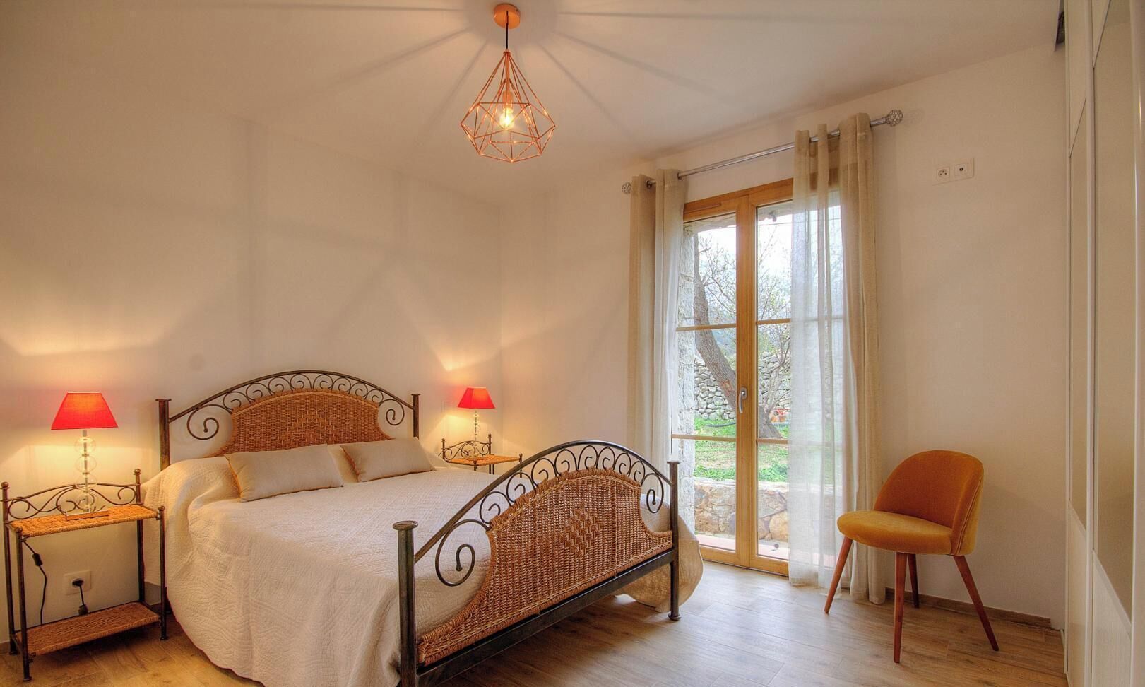 A bedroom with a bed, two bedside lamps, a chair, and a window with curtains.