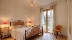 Ein Schlafzimmer mit einem Bett, zwei Nachttischlampen, einem Sessel und einem Fenster mit Vorhängen.