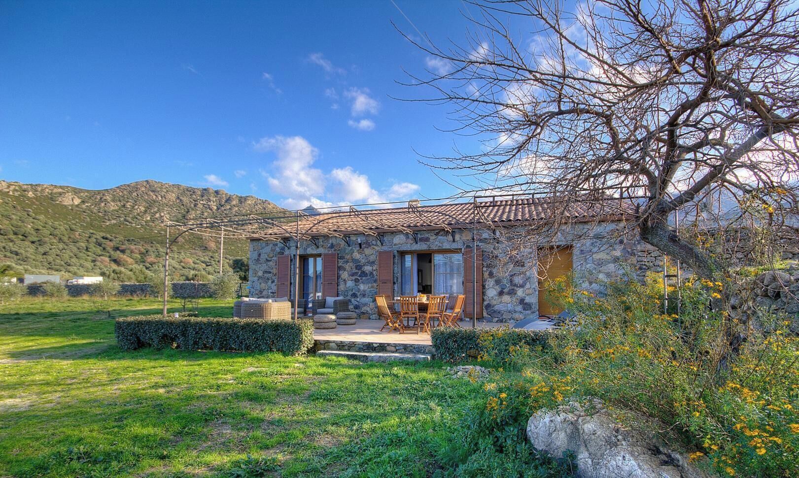 A stone house with a tiled roof, outdoor seating, and a view of the surrounding landscape.