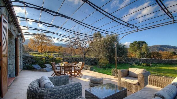 Eine überdachte Terrasse im Freien mit Rattanmöbeln, einem Tisch und Stühlen.