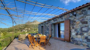 Ein Steinhaus mit überdachter Terrasse, Gartenmöbeln und Blick auf die Landschaft.