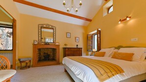Ein Schlafzimmer mit Kamin, einem Bett mit Kissen, einem Holzstuhl und einer Chandelier.