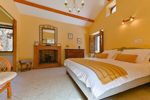 Ein Schlafzimmer mit Kamin, einem Bett mit Kissen, einem Holzstuhl und einer Chandelier.