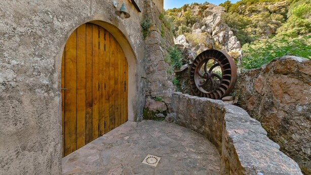 Ein rustikales Steinhaus mit Holztür und einem großen Wasserrad.