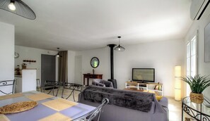 A living room with a sofa, a dining table with chairs, a TV, a lamp, and a window. - The San Michele - SISCO (SISCO)
