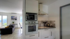 A modern kitchen with a built-in microwave, oven, and stove, a dining area with a table and chairs, and a balcony with a view. - The San Michele - SISCO (SISCO)