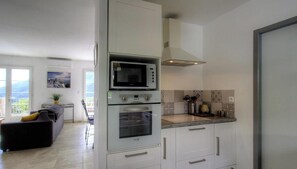 A modern kitchen with a built-in microwave, oven, and stove, a dining area with a table and chairs, and a balcony with a view. - The San Michele - SISCO (SISCO)