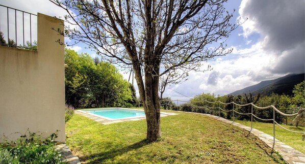 A swimming pool surrounded by a grassy area, a tree, and a mountainous landscape. - The San Michele - SISCO (SISCO)