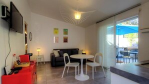 Ein modernes Wohnzimmer mit einer Couch, zwei weißen Sesseln, einem kleinen Tisch, einem roten Schrank, einem Flachbildfernseher und einer Deckenleuchte.