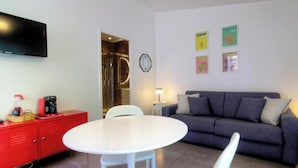 Ein modernes Wohnzimmer mit grauem Sofa, weißem runden Tisch, rotem Stauraum und einem flachbildfernseher an der Wand.