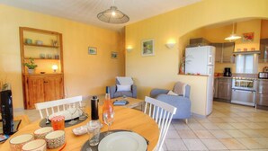 A dining area with a table set for four, a sofa, and a kitchen in the background. - Les oliviers 1 - SOLLACARO (SOLLACARO)